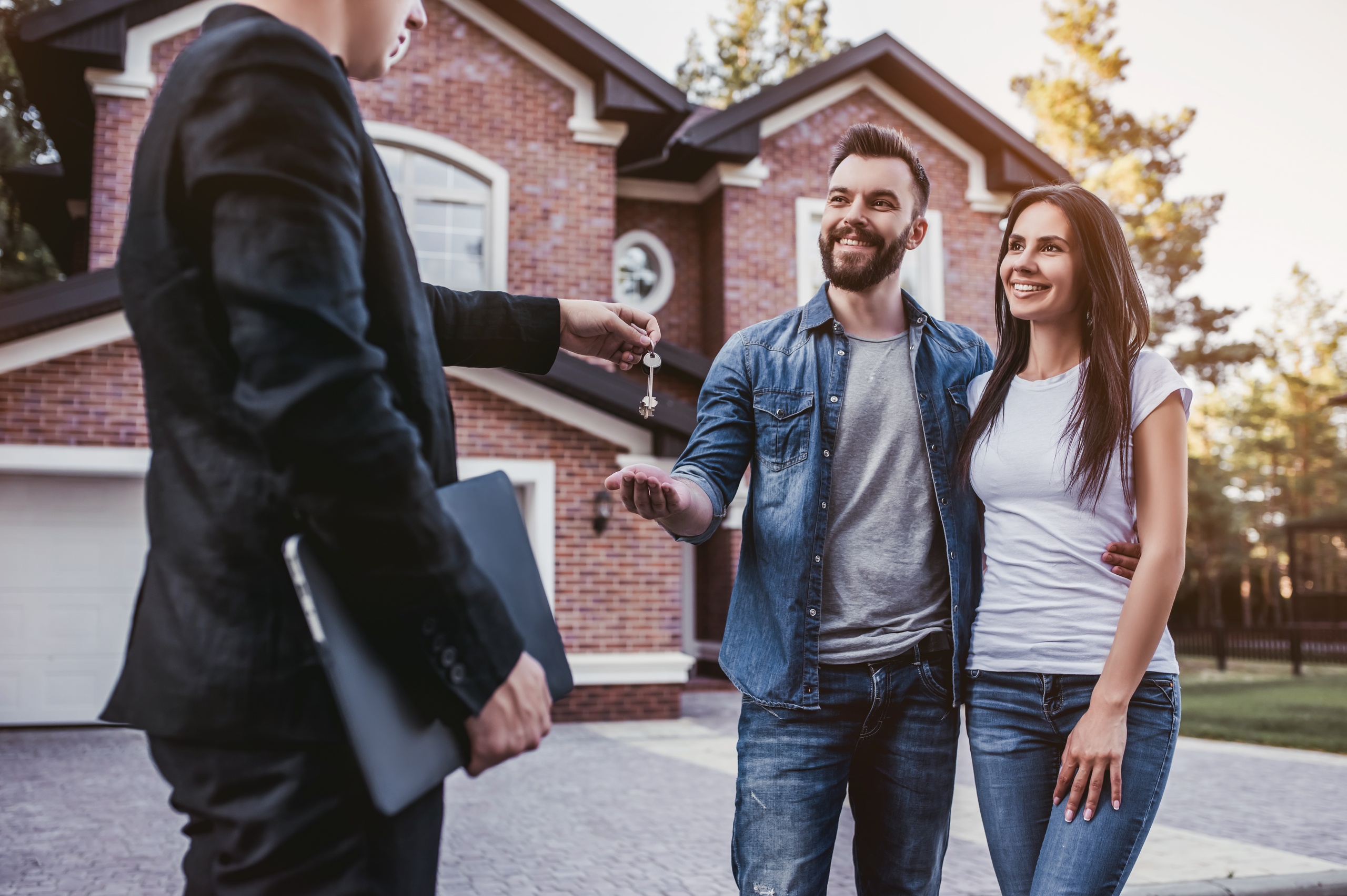 Happy couple is taking keys for their new house from broker and smiling